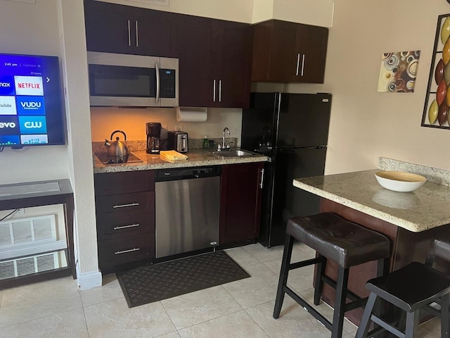 kitchen featuring a kitchen breakfast bar, dark brown cabinets, sink, black appliances, and light tile patterned floors