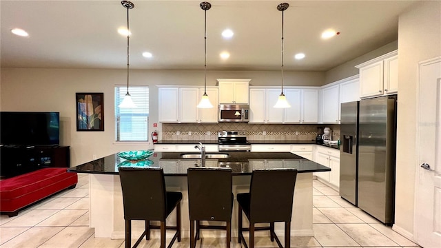 kitchen with white cabinets, appliances with stainless steel finishes, a kitchen island with sink, and pendant lighting