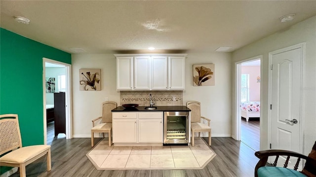 bar featuring white cabinets, backsplash, light hardwood / wood-style flooring, and beverage cooler