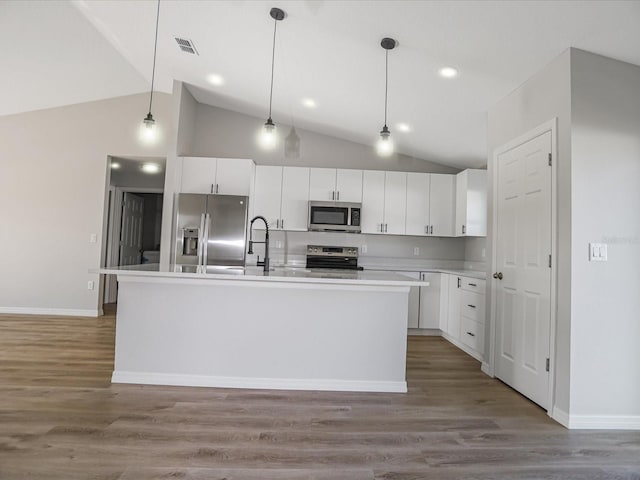 kitchen with hardwood / wood-style flooring, stainless steel appliances, pendant lighting, and an island with sink