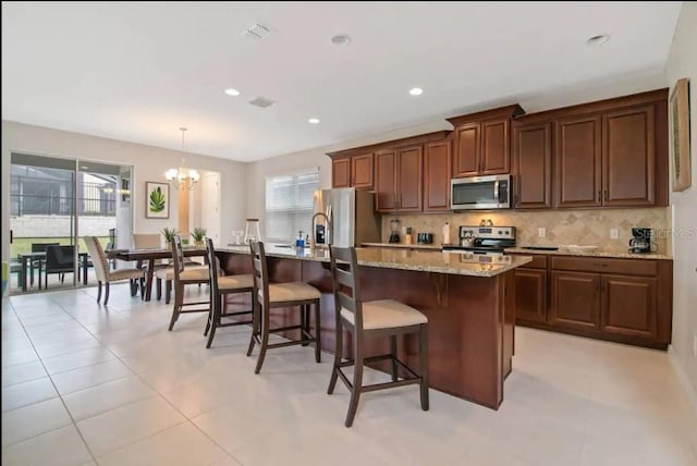 kitchen featuring stainless steel appliances, a kitchen island with sink, a wealth of natural light, and decorative light fixtures