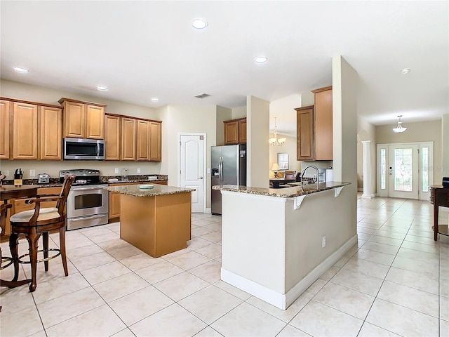 kitchen with a kitchen breakfast bar, kitchen peninsula, stainless steel appliances, dark stone countertops, and an inviting chandelier