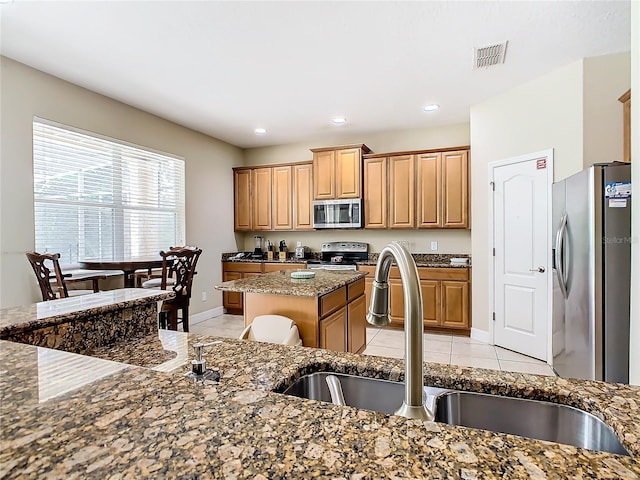 kitchen featuring a kitchen island, dark stone counters, sink, light tile patterned floors, and appliances with stainless steel finishes