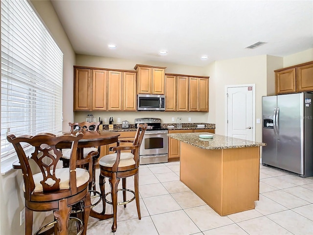 kitchen featuring a center island, light stone countertops, stainless steel appliances, and light tile patterned floors