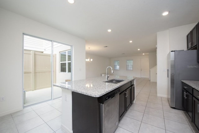 kitchen with appliances with stainless steel finishes, sink, light tile patterned floors, light stone counters, and a center island with sink