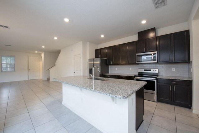 kitchen with sink, light stone counters, a center island with sink, stainless steel appliances, and backsplash