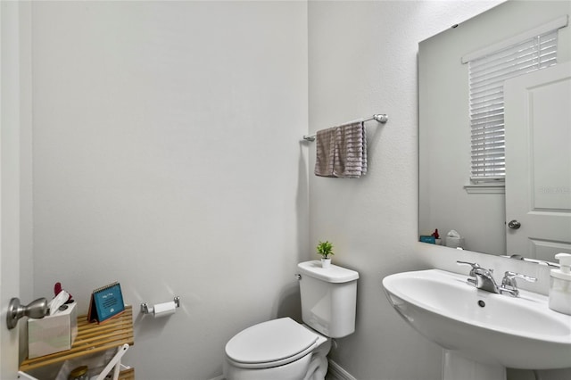 half bathroom featuring toilet, baseboards, and a sink