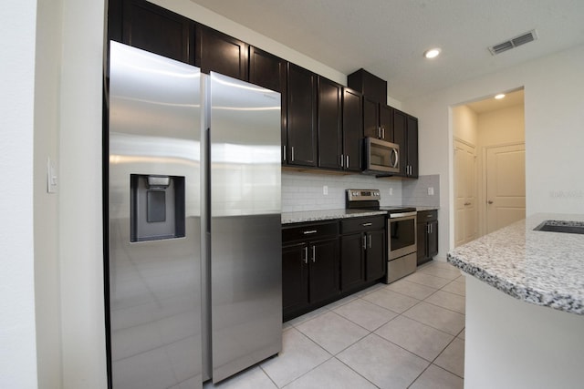 kitchen with visible vents, light stone counters, appliances with stainless steel finishes, light tile patterned floors, and decorative backsplash