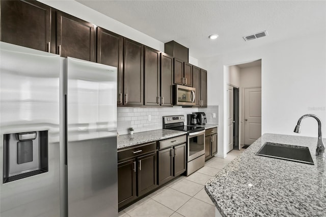 kitchen with visible vents, a sink, tasteful backsplash, appliances with stainless steel finishes, and light stone countertops