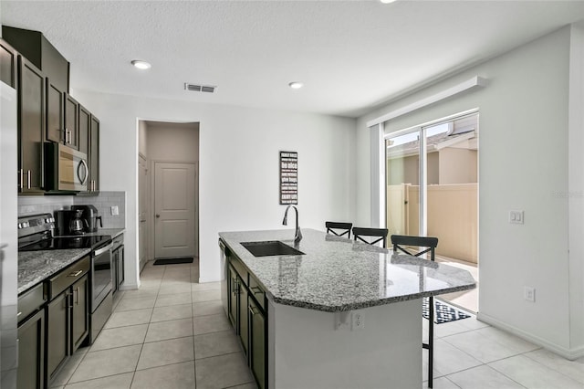 kitchen with visible vents, a kitchen island with sink, a sink, stainless steel appliances, and a breakfast bar area