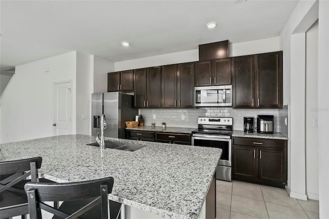 kitchen featuring dark brown cabinets, backsplash, light tile patterned floors, stainless steel appliances, and a sink