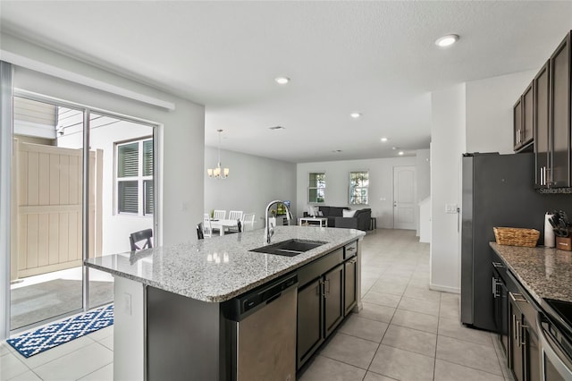 kitchen with a sink, light stone counters, appliances with stainless steel finishes, and an island with sink