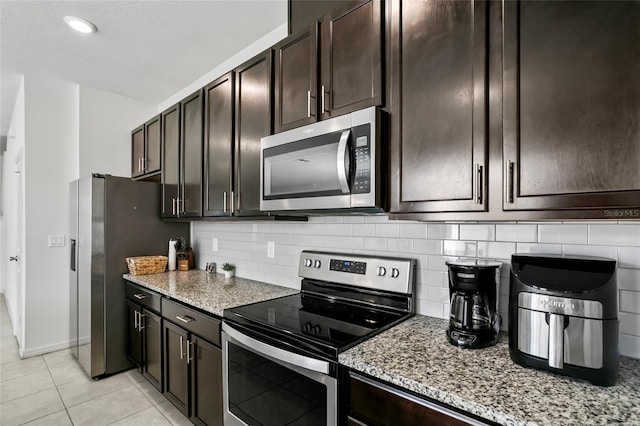 kitchen with dark brown cabinetry, light stone counters, decorative backsplash, light tile patterned floors, and appliances with stainless steel finishes