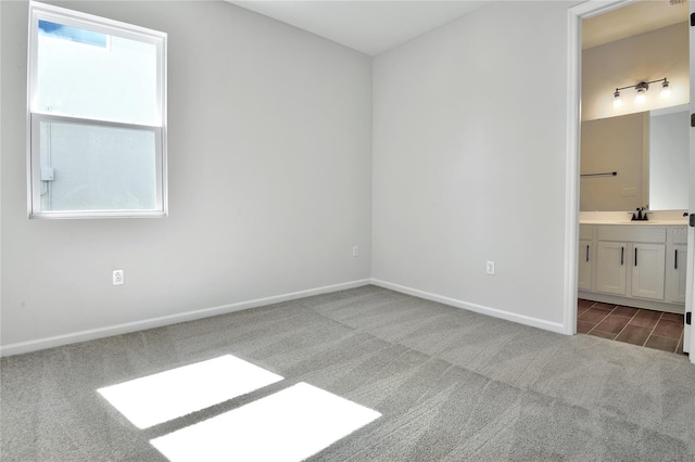 unfurnished bedroom featuring dark colored carpet, ensuite bath, and sink