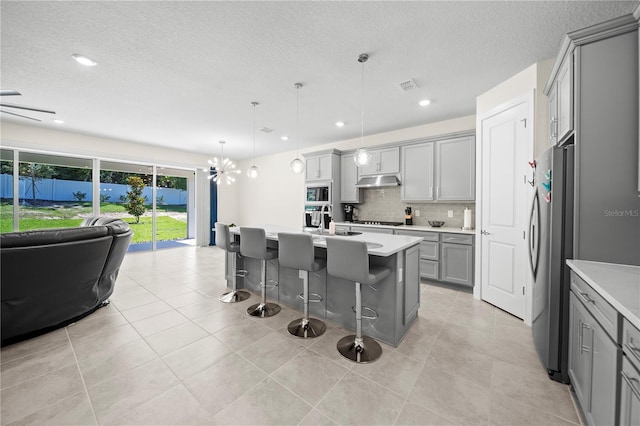 kitchen with hanging light fixtures, tasteful backsplash, an island with sink, gray cabinets, and a breakfast bar