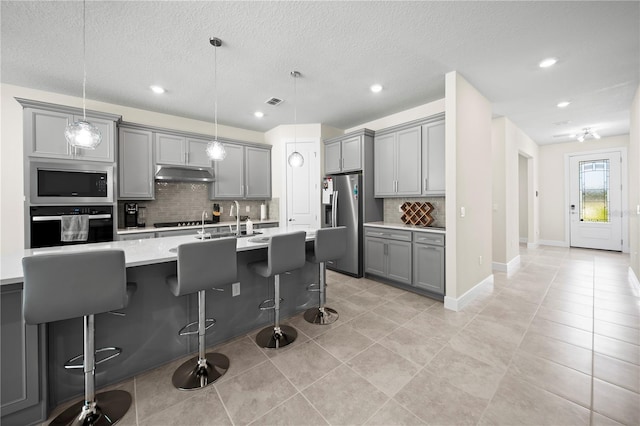 kitchen with appliances with stainless steel finishes, decorative light fixtures, backsplash, and a center island with sink