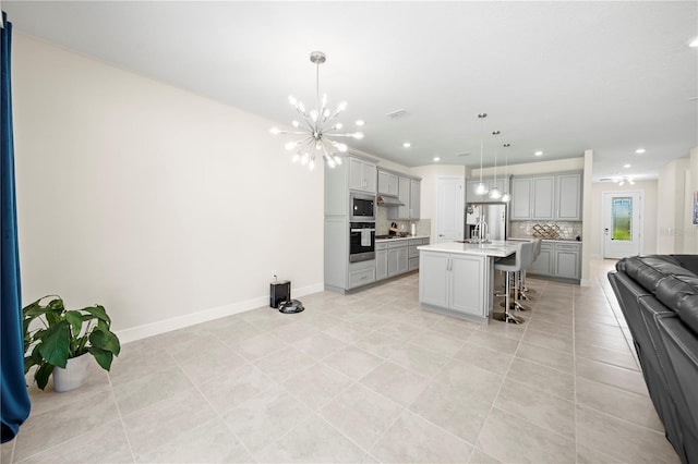 kitchen featuring backsplash, hanging light fixtures, a breakfast bar area, an island with sink, and appliances with stainless steel finishes