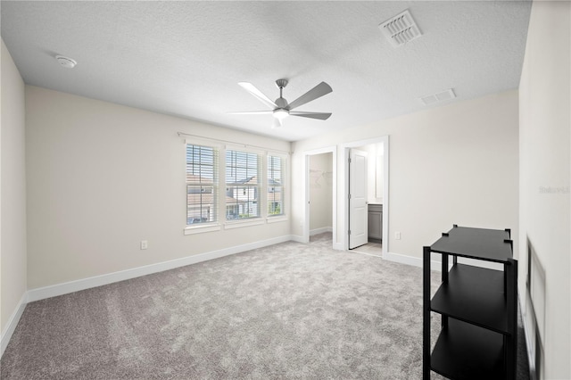 unfurnished bedroom featuring a closet, ceiling fan, a walk in closet, light carpet, and a textured ceiling