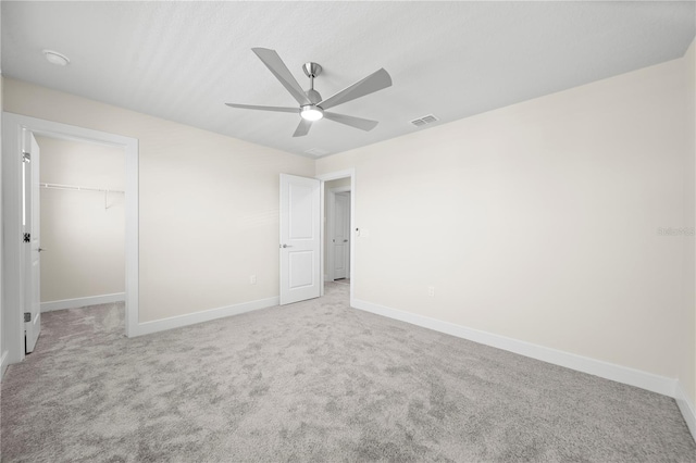 unfurnished bedroom featuring light carpet, a spacious closet, ceiling fan, and a closet