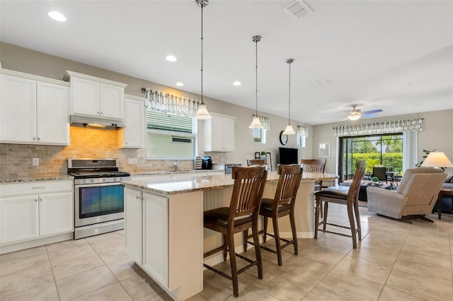 kitchen with pendant lighting, white cabinets, gas range, ceiling fan, and a kitchen island