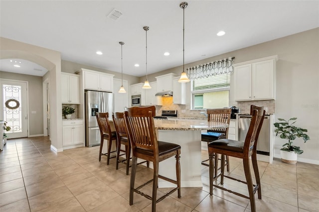 kitchen featuring a center island, hanging light fixtures, decorative backsplash, white cabinets, and appliances with stainless steel finishes