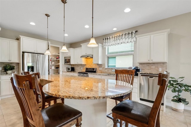 kitchen with light stone countertops, white cabinetry, stainless steel appliances, pendant lighting, and a kitchen island