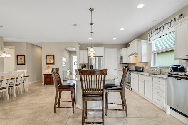 kitchen with white cabinets, a kitchen island, light stone countertops, and stainless steel appliances