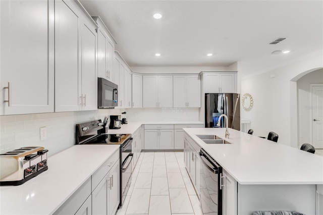 kitchen featuring decorative backsplash, appliances with stainless steel finishes, a kitchen breakfast bar, sink, and a center island with sink