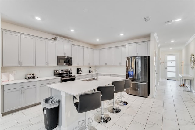 kitchen featuring sink, a breakfast bar area, ornamental molding, appliances with stainless steel finishes, and a kitchen island with sink