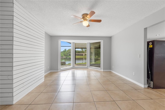 unfurnished room with a textured ceiling, a water view, ceiling fan, and light tile patterned flooring