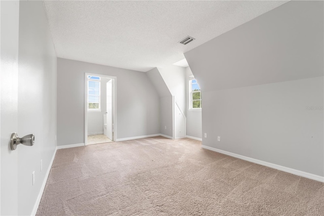 bonus room featuring light carpet, vaulted ceiling, and a textured ceiling