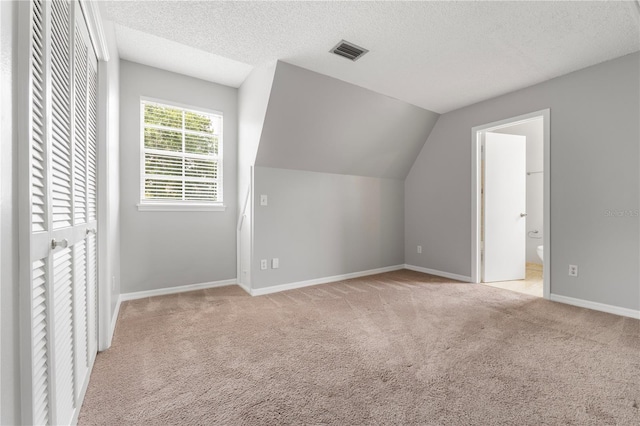 bonus room with vaulted ceiling, light carpet, and a textured ceiling