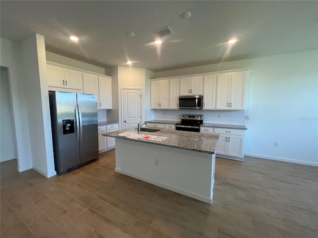 kitchen with white cabinetry, stainless steel appliances, a kitchen island with sink, light stone counters, and sink