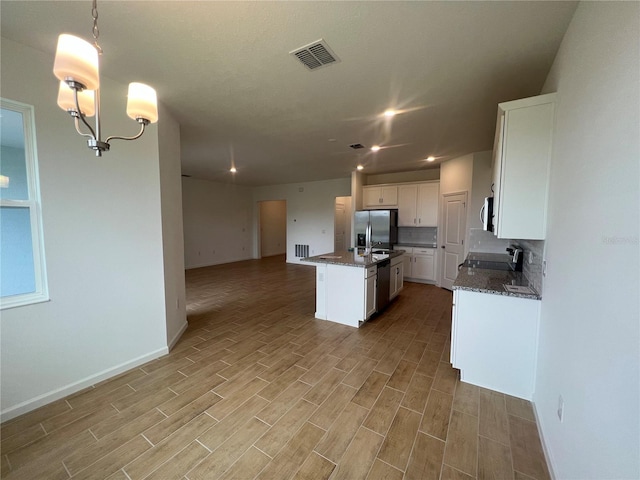 kitchen with decorative light fixtures, white cabinetry, stainless steel appliances, sink, and a kitchen island with sink