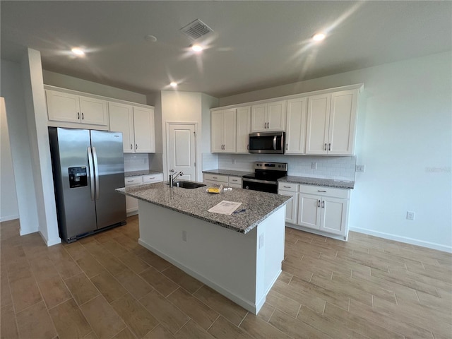 kitchen featuring stone counters, stainless steel appliances, white cabinets, and an island with sink