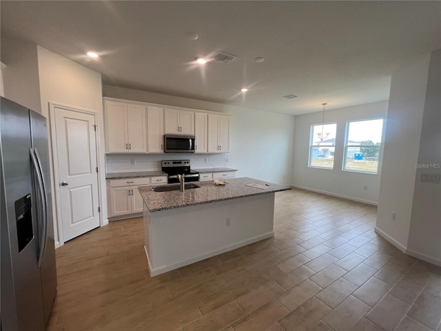 kitchen featuring light stone countertops, white cabinets, stainless steel appliances, backsplash, and a kitchen island with sink