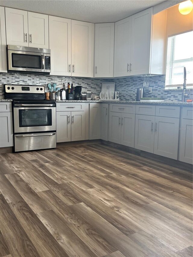 kitchen with light stone counters, tasteful backsplash, white cabinetry, dark wood-type flooring, and appliances with stainless steel finishes