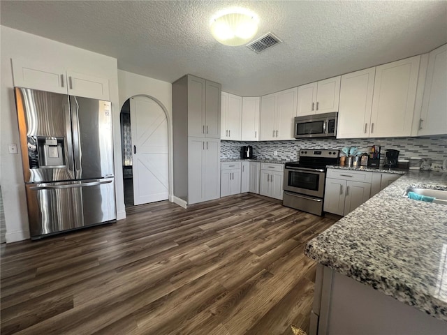 kitchen featuring a textured ceiling, dark hardwood / wood-style flooring, stainless steel appliances, stone counters, and tasteful backsplash