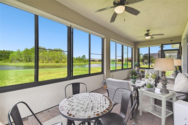 sunroom with ceiling fan and a water view