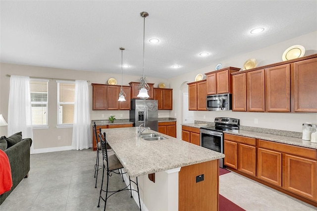 kitchen with stainless steel appliances, an island with sink, light tile floors, decorative light fixtures, and a kitchen bar