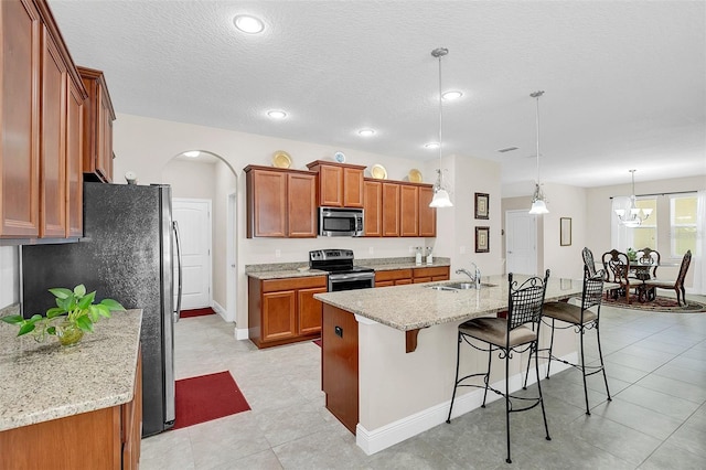 kitchen featuring appliances with stainless steel finishes, an island with sink, decorative light fixtures, sink, and light tile flooring