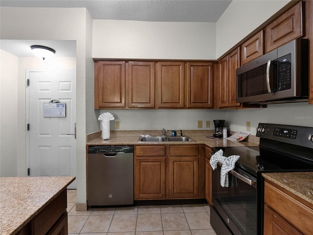 kitchen with sink, stone counters, light tile floors, and appliances with stainless steel finishes