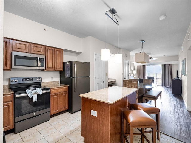 kitchen featuring a kitchen island, stainless steel appliances, hanging light fixtures, ceiling fan, and a breakfast bar