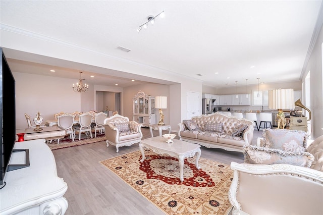 living room with ornamental molding, light hardwood / wood-style floors, an inviting chandelier, and rail lighting