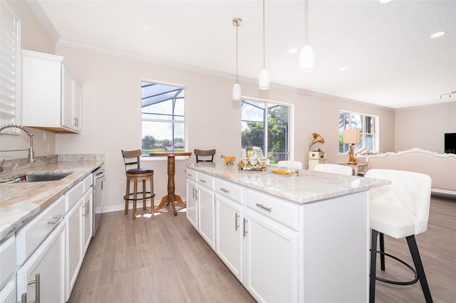 kitchen featuring a kitchen breakfast bar, hanging light fixtures, a kitchen island, light hardwood / wood-style flooring, and sink