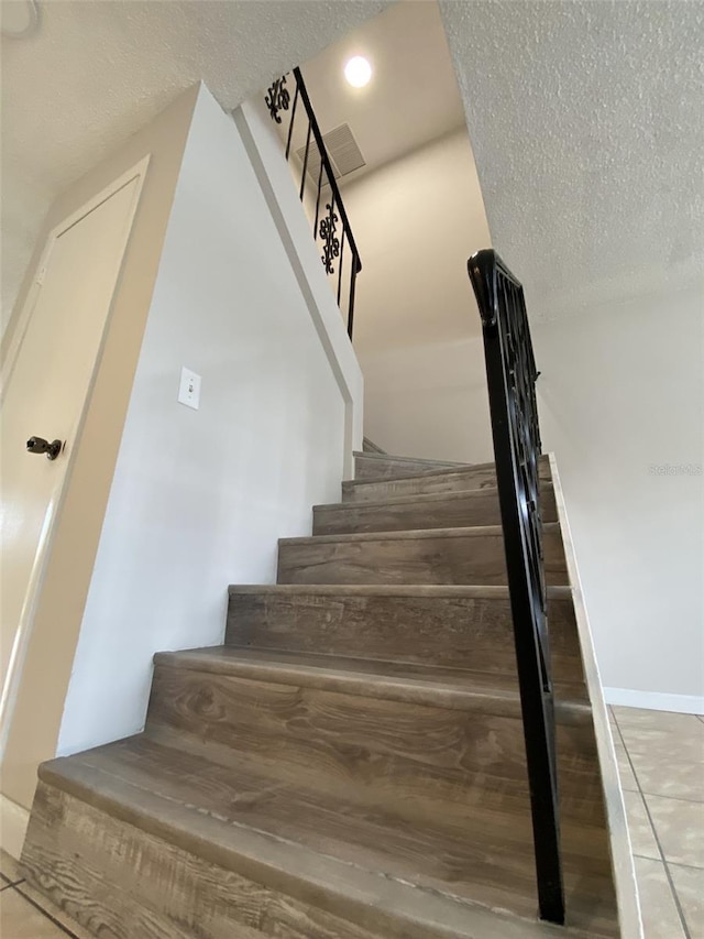 stairway with tile patterned floors and a textured ceiling