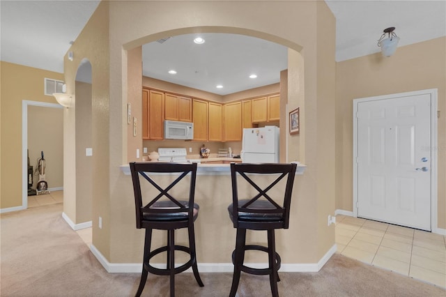 kitchen with light brown cabinets, white appliances, light colored carpet, kitchen peninsula, and a kitchen breakfast bar