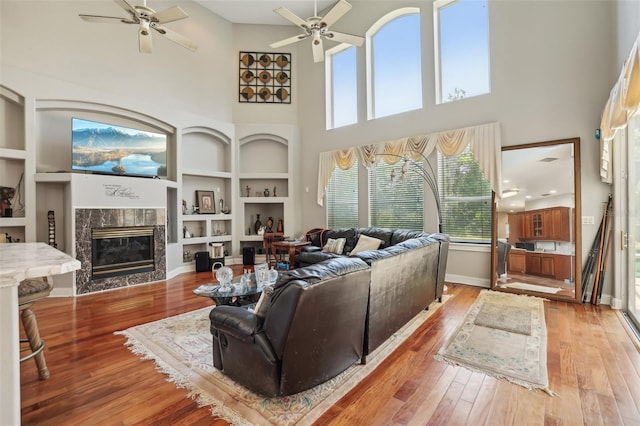 living room featuring built in shelves, a tile fireplace, hardwood / wood-style floors, a high ceiling, and ceiling fan