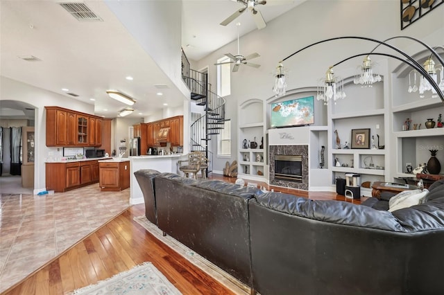 living room featuring light hardwood / wood-style floors, a fireplace, ceiling fan with notable chandelier, built in features, and a towering ceiling