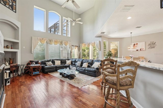 living room featuring a high ceiling, dark wood-type flooring, built in features, and ceiling fan with notable chandelier